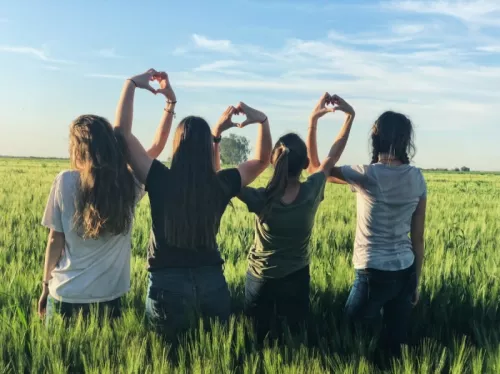 Four women in a field making heart hands