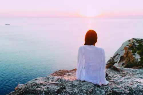 Woman Sat On Cliff Looking Towards Horizon